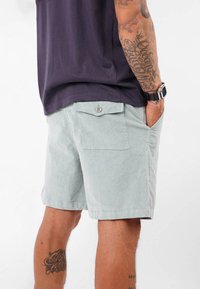 Shorts en velours côtelé vert clair avec une coupe droite, dotés de poches latérales et d'une poche arrière à bouton. Le tissu présente une surface texturée.