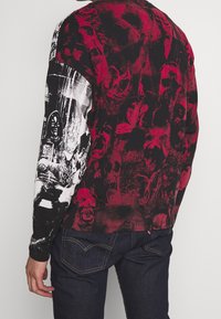 Long-sleeve shirt featuring a black and red design with skull patterns and graphics on the back, made of lightweight fabric.