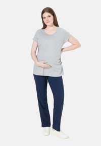 Grå kortärmad gravid topp med vita prickar, kombinerad med marinblå byxor. Outfiten kompletteras av vita sneakers.