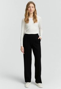 Sorte skræddersyede bukser med høj talje, forlommer og lige ben, kombineret med en langærmet hvid top. Glat stofstruktur.