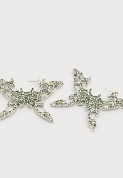 Ασημένια σκουλαρίκια με σχέδιο λουλουδιού, διακοσμημένα με πράσινες στρας. Διαθέτουν πολύπλοκες λεπτομέρειες και αιχμηρές διακοσμήσεις.
