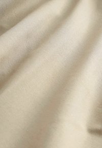 Tissu beige lisse avec une texture fine de tissage visible et des plis doux créant des ombres délicates.