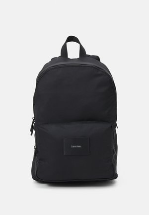 Černý batoh z odolné tkaniny, vybavený přední kapsou, zipovým zavíráním a nášivkou s logem. Jednoduchý design s nastavitelnými popruhy.