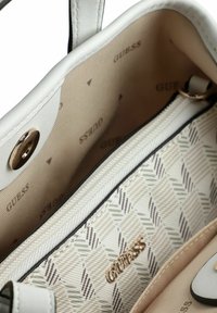 Sac à main blanc avec un intérieur texturé arborant un motif géométrique en gris et beige, quincaillerie dorée et logo de la marque visible à l'intérieur.