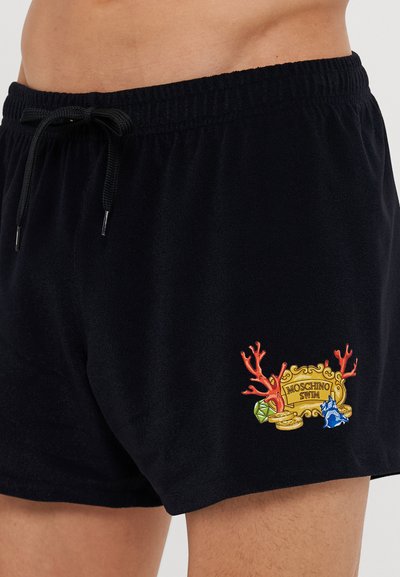 Melnas peldbikses, kas izgatavotas no mīksta auduma, ar izšūtu dizainu, kas attēlo korāļus, dārgakmens un tekstu "Moschino Swim" kreisajā augšstilbā.