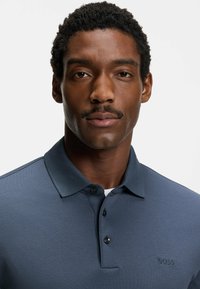 Męska koszulka polo w ciemnym niebieskim kolorze. Posiada klasyczny kołnierzyk, plisę zapinaną na trzy guziki oraz subtelne haftowane logo. Wykonana z miękkiej, teksturowanej tkaniny.