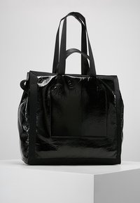 Czarna torba na ramię o błyszczącej powierzchni, z dwiema ramiączkami i przednią kieszenią. Prostokątny kształt z fakturowaną powierzchnią.