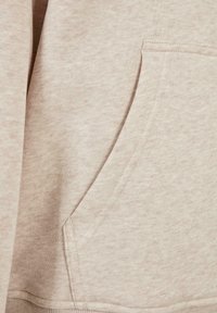 Lys beige sweatshirt med et mykt, teksturert stoff. Har en kengurulomme foran og ribbestrikkede mansjetter ved søm og ermer.