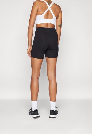 Shorts de sport noirs en tissu extensible, associés à un haut de sport blanc. Les shorts présentent une taille haute et une texture lisse.