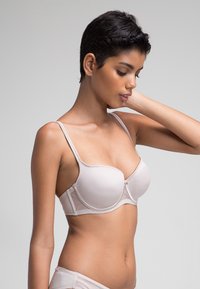 Sujetador acolchado color beige claro con tirantes ajustables y una textura suave. Presenta un cierre seguro en la parte delantera, ofreciendo un diseño sin costuras.