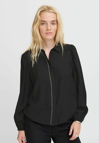 Black button-up blouse with puffed sleeves and a textured fabric. Features a front placket with small, decorative buttons and a relaxed fit.