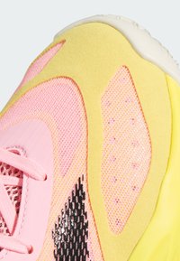 Sneaker med en pink mesh-overdel og gule suede-accenter, sorte gummidetaljer og pink snørebånd. Tekstureret overflade overalt.