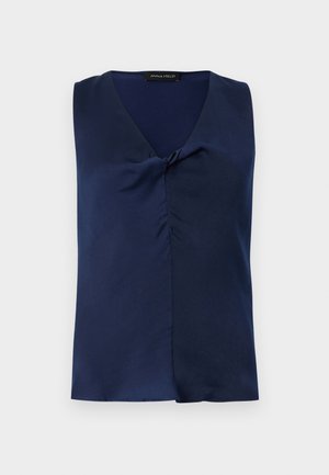 Μπλούζα χωρίς μανίκια σε ναυτικό μπλε χρώμα με λαιμόκοψη σε σχήμα V και διακριτική πτυχή εμπρός, διπλωμένη προσεκτικά επάνω σε απλό φωτεινό φόντο.