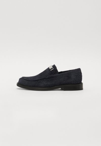 Pantofii slip-on de culoare bleumarin, cu un superior texturat și pufos, o talpă neagră și un accent argintiu pe curea. Design cu vârf rotund.