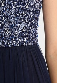 Marinblå klänning med en paljettbehå som har olika nyanser av blått och silver, som övergår till en lager av tyllkjol.