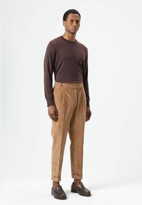 Brown long-sleeve shirt, beige corduroy pants, and dark loafers. Tapered pants with front pleats, smooth texture, and rolled cuffs.