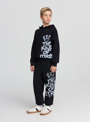 Felpa nera e pantaloni da jogging con grande testo bianco "THE KING OF STREET" e grafica di una corona, realizzati in tessuto morbido e confortevole.