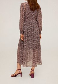 Floralmaxikleid aus durchscheinendem schwarzem Stoff mit rosa und lila Blumen. Verfügt über lange Puffärmel und einen gestuften Rock. Kombiniert mit lila Absatzsandalen.