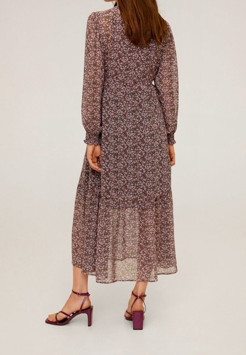 Floralmaxikleid aus durchscheinendem schwarzem Stoff mit rosa und lila Blumen. Verfügt über lange Puffärmel und einen gestuften Rock. Kombiniert mit lila Absatzsandalen.