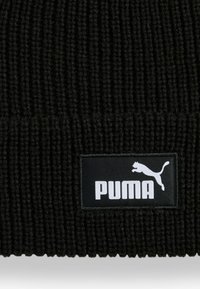Berretto lavorato a maglia nero con una texture a coste e un'etichetta rettangolare nera che mostra il logo bianco "PUMA" e il design del gatto saltante.