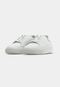 Hvite sneakers i lær med flat såle, perforert tådesign og hvite lisser. Har en diskret logotagg på siden.