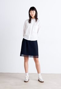 Camisa de botones blanca a rayas combinada con una falda negra plisada con dobladillo transparente, llevada con zapatillas altas blancas y calcetines blancos.