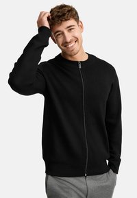 Cárdigan negro con cremallera, cuello redondo, puños y dobladillo de canalé. Textura de punto suave, diseño sencillo, adecuado para un uso casual.