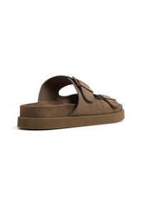 Brown suede slide sandals with a flat profile, featuring two oversized straps and stitching accents along the edges.