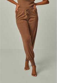 Brown knit jogger pants with a drawstring waist, tapered ankles, and side pockets. Soft texture, relaxed fit, and smooth finish.
