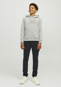 Grijze hoodie met logo en kangoeroezak, gecombineerd met donkerblauwe cargobroek. Witte sneakers maken de casual outfit compleet.