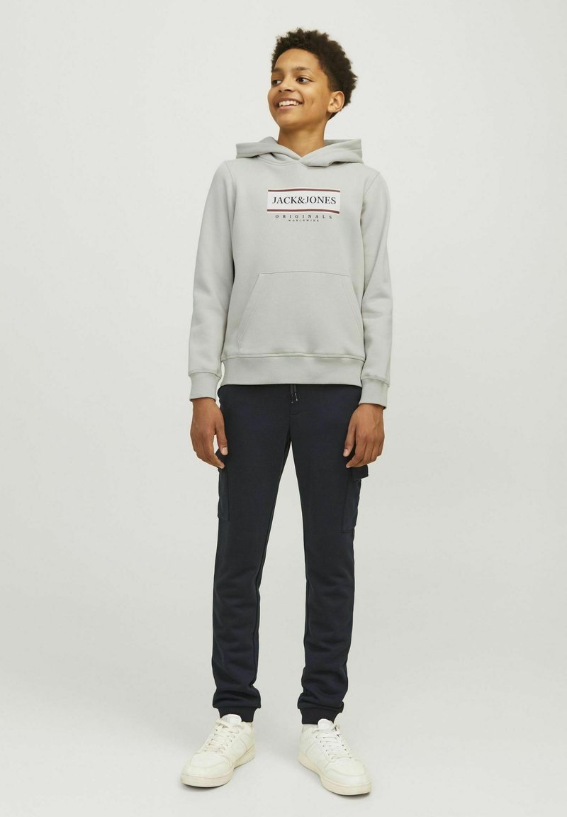 Grijze hoodie met logo en kangoeroezak, gecombineerd met donkerblauwe cargobroek. Witte sneakers maken de casual outfit compleet.