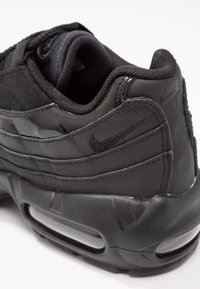 Nike Air Max 95-sko i svart, med en strukturerad ovandel, mesh-detaljer och en synlig luftkudde i den kraftiga sulan.