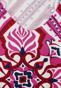 V-ringad blommig topp med ett livfullt mönster i rosa, röd och marinblått. Tyget är mjukt med intrikata grafiska mönster och kontrasterande former.
