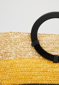 Woven straw bag featuring yellow and natural tones, a round black handle, and textured patterns on the surface.