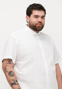 Cămașă albă cu mânecă scurtă, cu guler clasic. Fabricată dintr-un material neted, cu un sistem de închidere cu nasturi în față și fără modele vizibile.