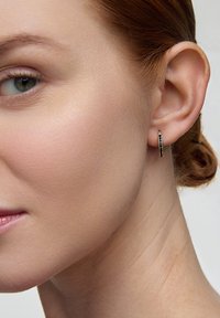 Złote kolczyki w kształcie obręczy o gładkim wykończeniu, z cienkim czarnym akcentem wzdłuż obwodu, prezentowane na uchu modelki.