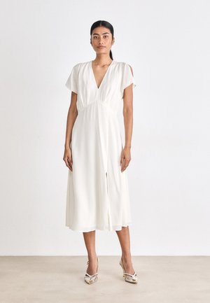 Robe midi blanche avec un décolleté en V profond, des manches courtes et des détails de découpe aux épaules. Elle présente une silhouette fluide et une fente à l'avant.