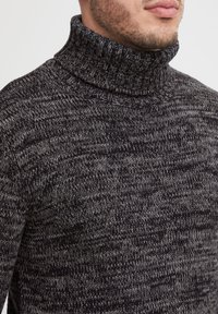 Grijs en zwart gebreide coltrui met een gestructureerd patroon en een geribbelde kraag. Close-up laat de zachtheid van het materiaal zien.
