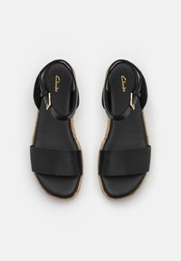 Sandales plates en cuir noir avec une large lanière avant, une lanière de boucle à la cheville, une semelle à détail en corde et le logo "Clarks" sur la semelle intérieure rembourrée.