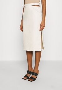 Knee-length cream cotton skirt, featuring a side slit and a smooth texture, paired with black slide-on heels.