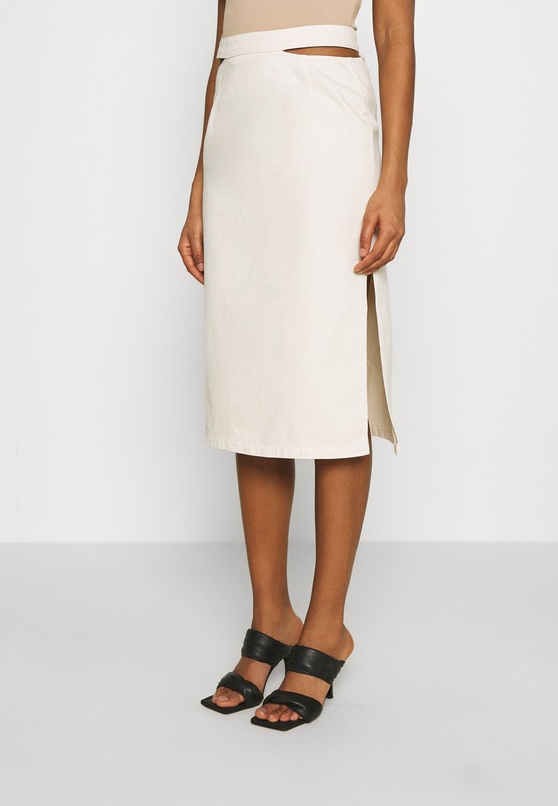 Knee-length cream cotton skirt, featuring a side slit and a smooth texture, paired with black slide-on heels.