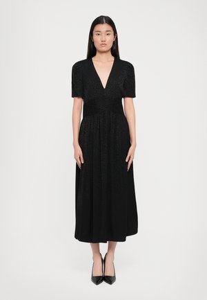 Vestido negro midi con mangas cortas, escote en V profundo, cinturilla plizada y patrón floral texturizado. Llevado con tacones negros de punta.
