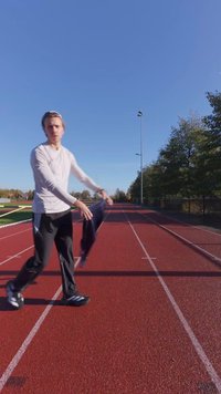 Spordiriietus hele pikkade varrukatega särgis ja tumedates pükstes; jooksurada punase pinnaga ja rohelise muruga kõrval; selge sinine taevas.