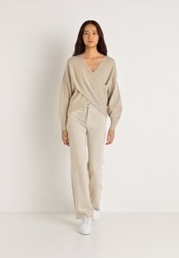 Μπεζ, ελαφρύ πλεχτό ζακέτα με V-λαιμόκοψη, συνδυασμένο με αντίστοιχες κομμένες παντελόνες και λευκά αθλητικά παπούτσια, με χαλαρή εφαρμογή.