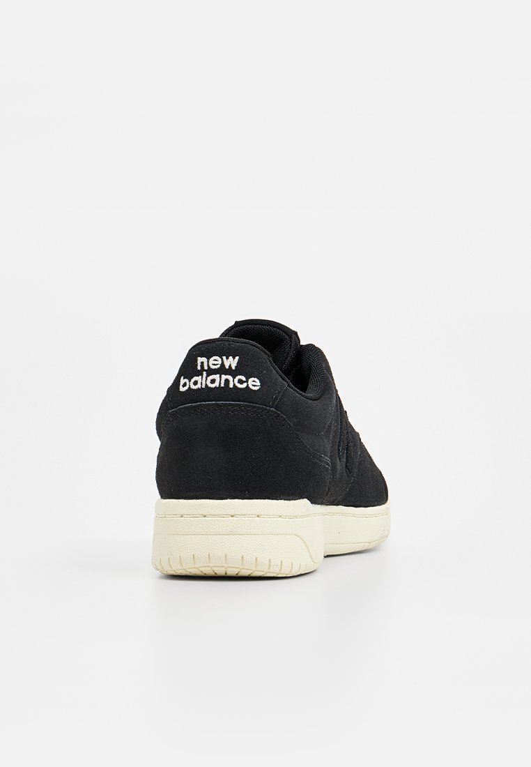 Zwarte suedine sneakers met een gestructureerde afwerking, voorzien van witte "New Balance" branding op de hak en een crèmekleurige rubberen zool.