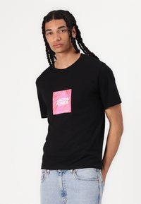 Musta puuvillatee, jossa on kirkkaan pinkki graafinen painatus "JACK & JONES", lyhyet hihat, pyöreä kaula-aukko ja rento leikkaus.