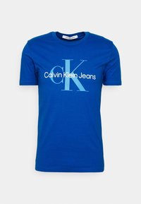 Camiseta de algodón azul con cuello redondo, mangas cortas y un estampado gráfico de "Calvin Klein Jeans" en texto blanco y azul claro.