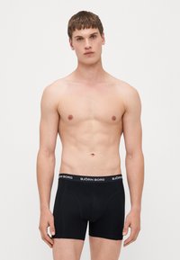 Schwarze Boxershorts mit einem flexiblen Bund, auf dem der Markenname "BJÖRN BORG" in Weiß steht. Hergestellt aus einem glatten Stoff mit einer enganliegenden Passform.