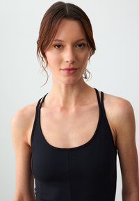 Schwarzes Sporttanktop mit Rundhalsausschnitt, dünnen Trägern und glattem, dehnbarem Stoff für Komfort und Bewegungsfreiheit.