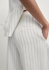 Wit gestreept linnen set met een korte mouw top en op maat gemaakte broek, met subtiele zwarte lijnen, een bescheiden zak en een ontspannen pasvorm.